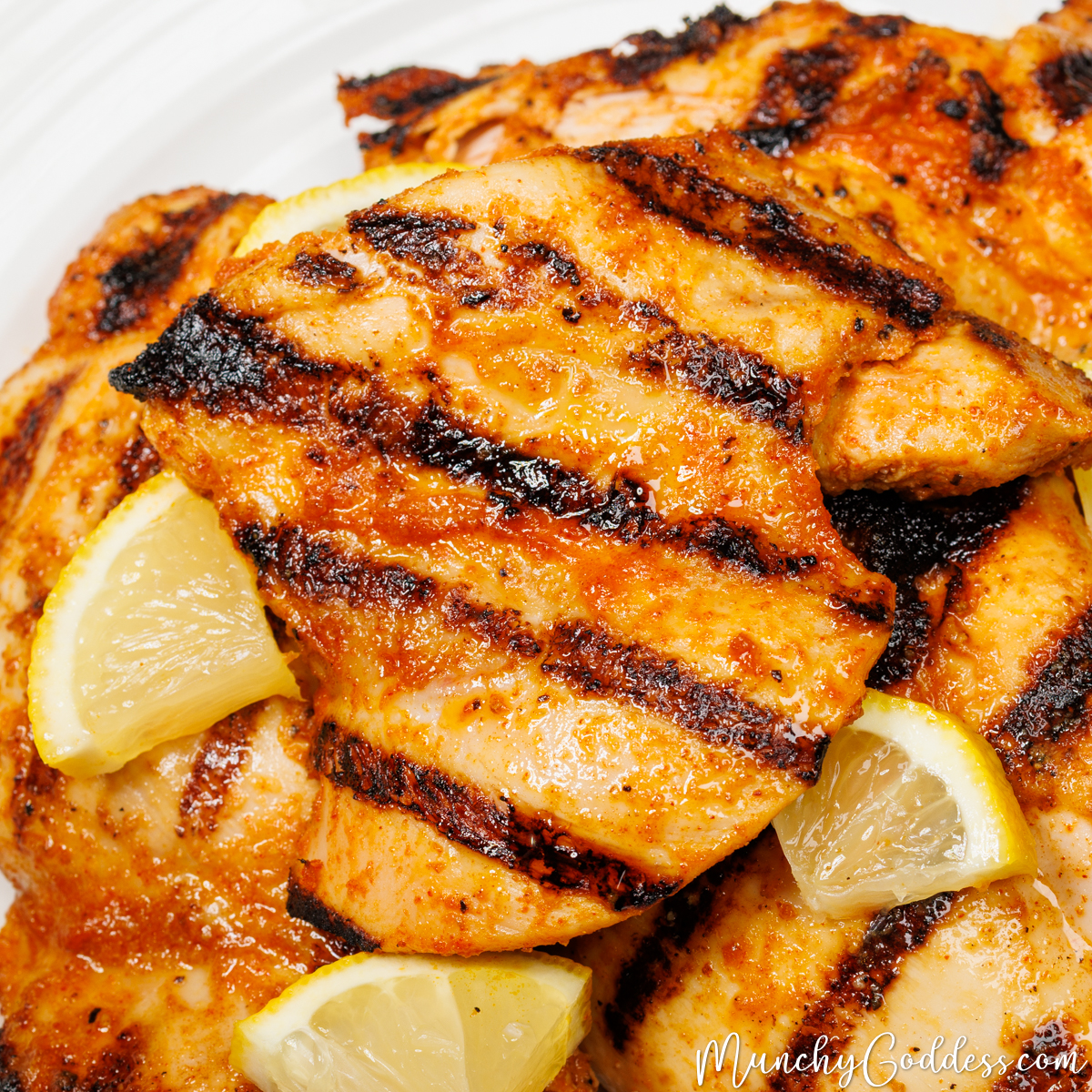 Grilled chicken thighs with dark, parallel sear marks garnished with lemon slices on an off-white plate.