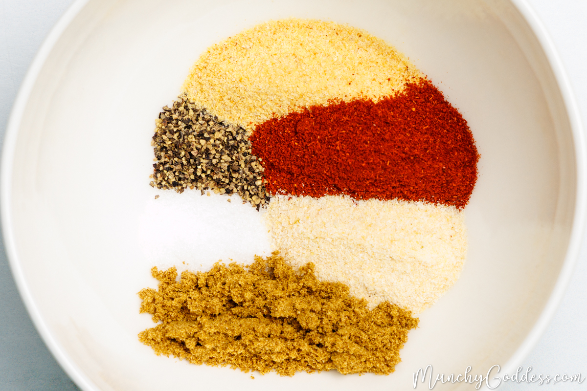 Salt, ground black pepper, smoked paprika, ground cumin, garlic powder, and onion powder neatly placed in an off-white bowl.