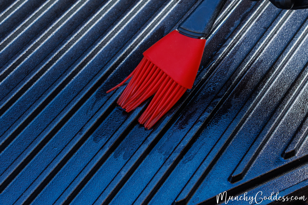 Cooking oil being brushed on the grilling surface with a red basting brush.