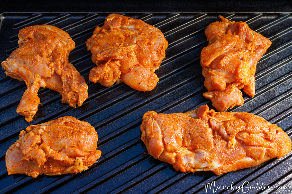 Seasoned chicken thighs on a black grilling surface smooth side down.