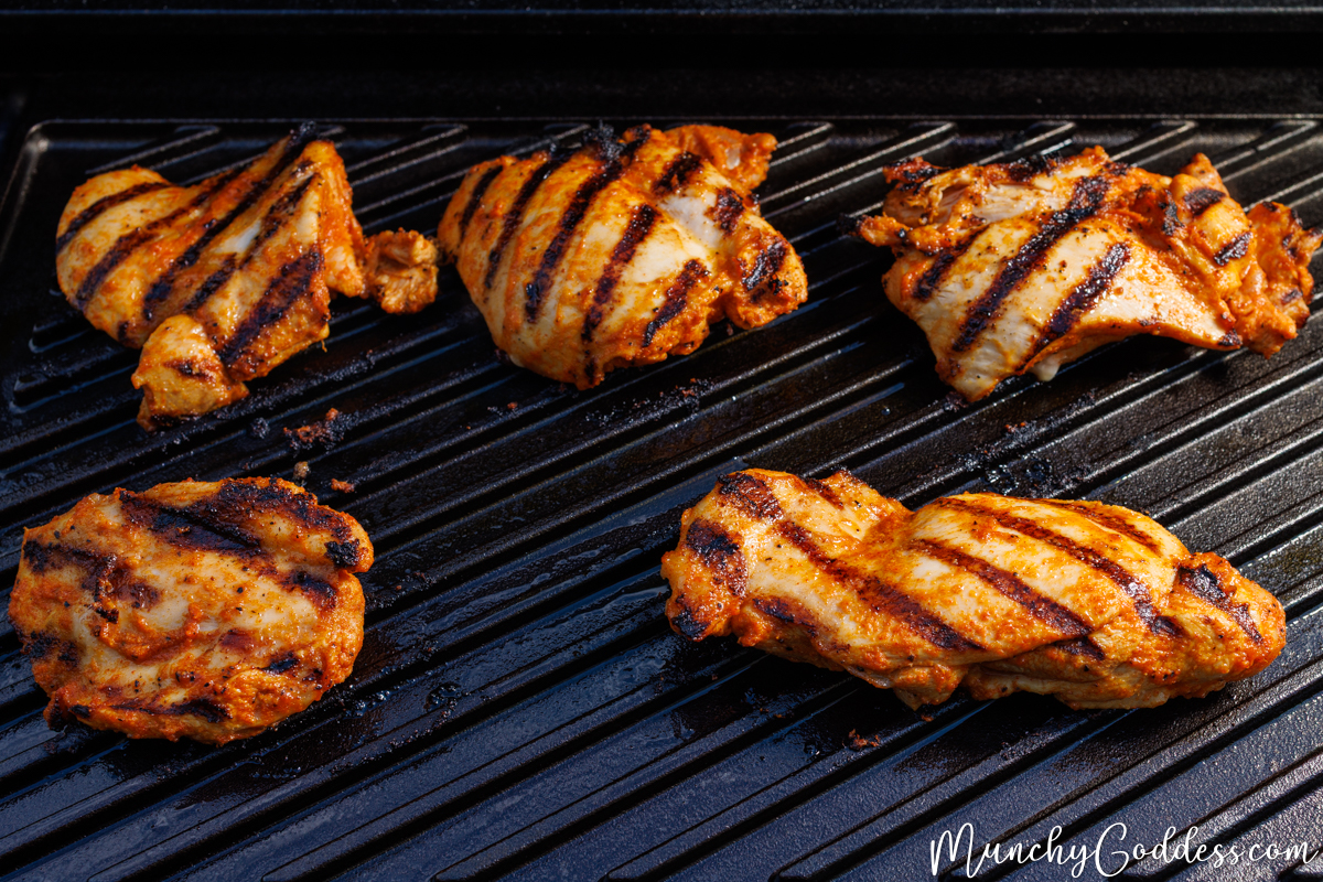 Grilled chicken thighs smooth side up with dark, parallel sear marks on a black grilling surface.