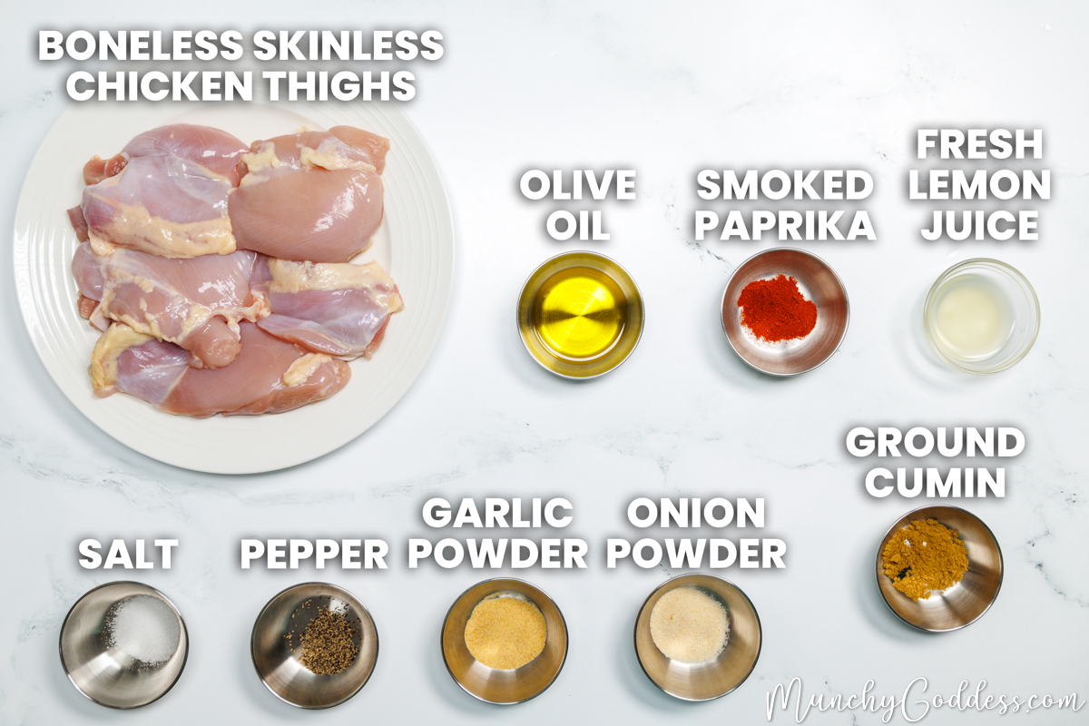 Grilled chicken thighs recipe ingredients in various dishes on a white marble surface: boneless skinless chicken thighs, olive oil, smoked paprika, fresh lemon juice, salt, ground black pepper, garlic powder, onion. powder, and ground cumin.