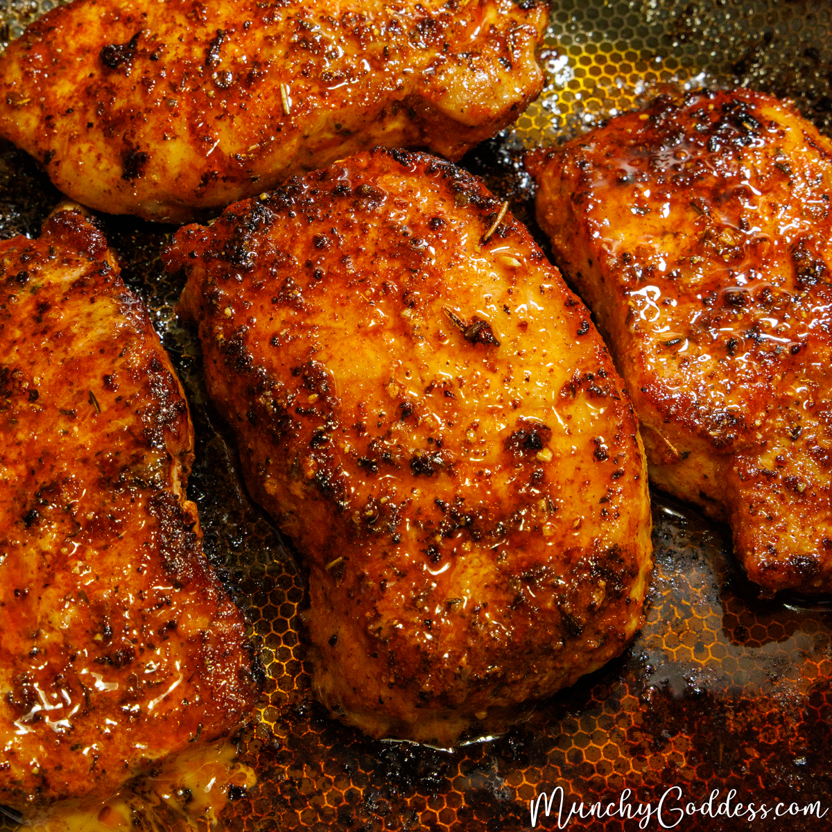 Golden brown pan-seared lemon pepper pork chops with a glistening glaze in a textured skillet with savory drippings.