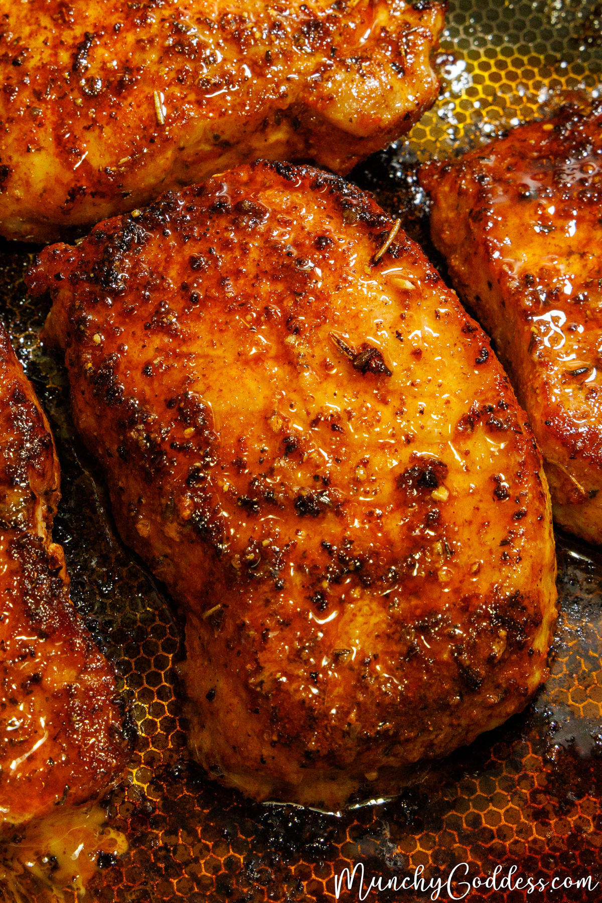 Golden brown lemon pepper pork chop with a glistening glaze, showing flecks of black pepper and dried herbs.