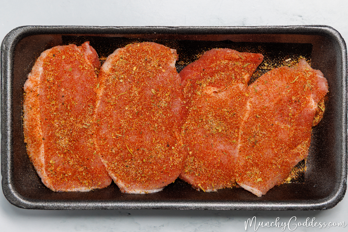 Boneless pork chops in a black foam meat tray evenly coated with a lemon pepper seasoning mixture.