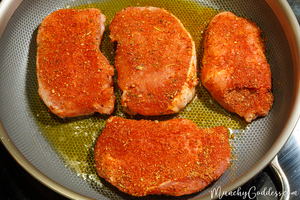 Seasoned boneless pork chops added to a heated honeycomb-textured skillet with olive oil.