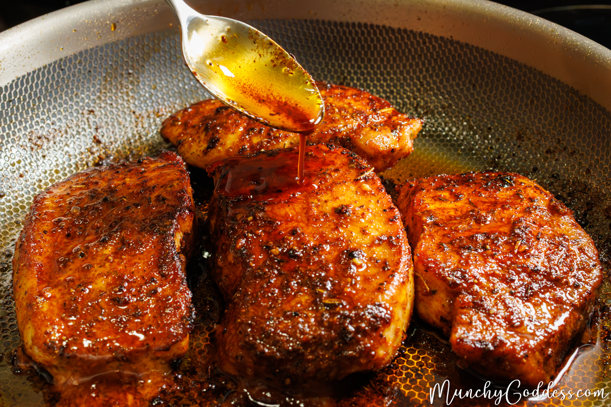 Golden brown boneless pork chops being basted with a rich, amber-colored butter sauce, highlighting the glossy glaze and savory herbs.