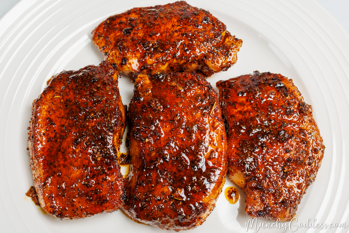 Lemon pepper pork chops drizzled with butter sauce resting on an off-white plate.