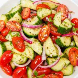 Cucumber tomato salad with halved cucumber slices, halved cherry tomatoes, and slices of red onion tossed in a homemade salad dressing.