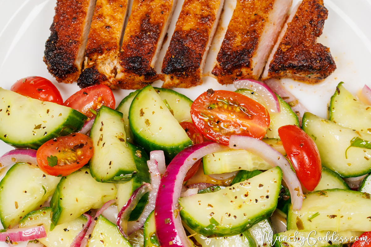 Sliced pork chop with cucumber tomato salad on a white plate.