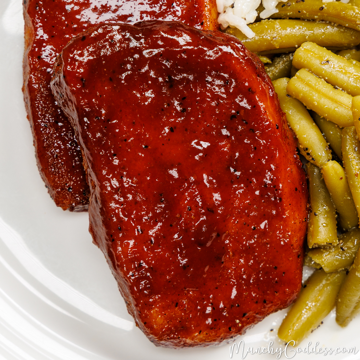 Baked bbq pork chops with green beans and rice on an off-white plate.