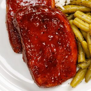 Baked bbq pork chops with green beans and rice on an off-white plate.