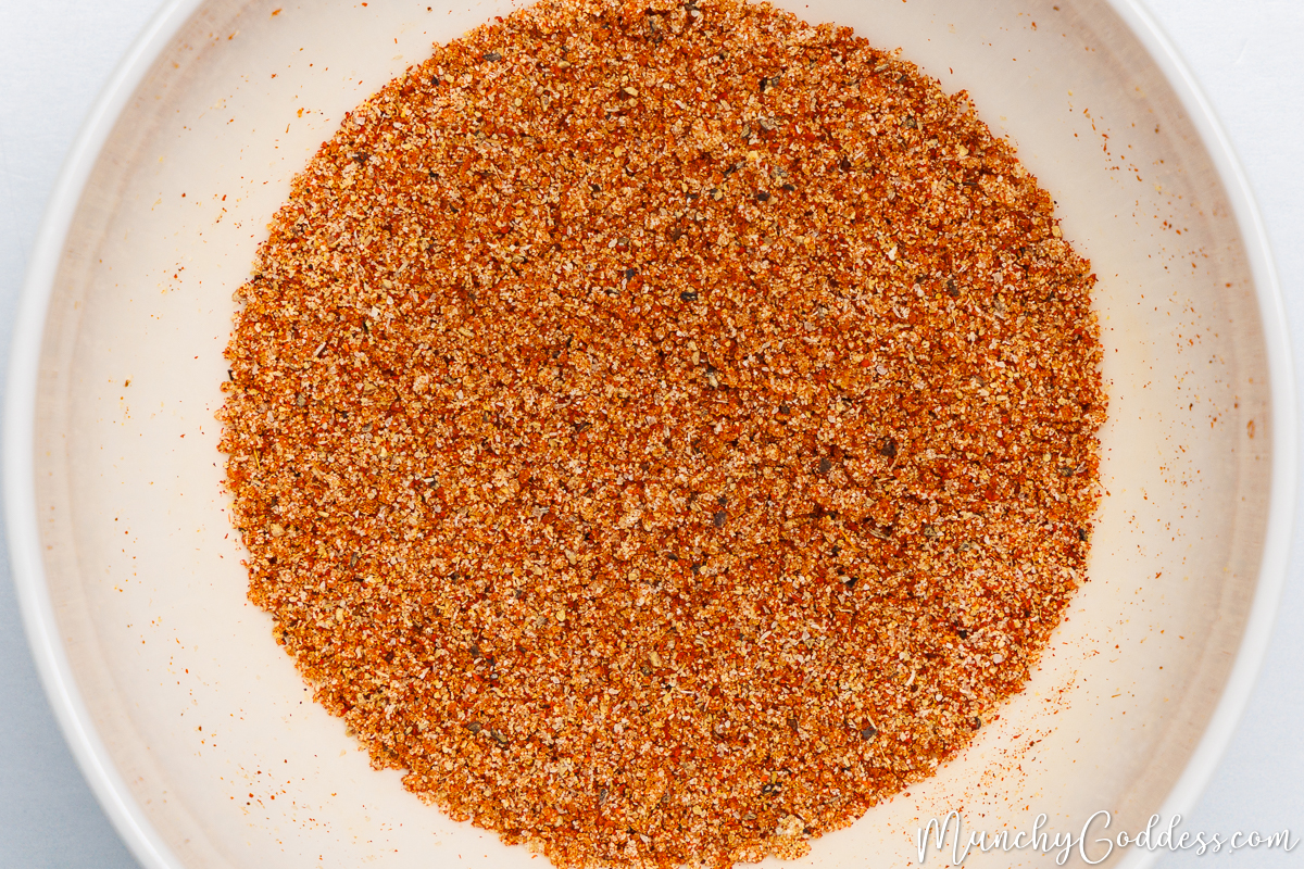 Salt, ground black pepper, onion powder, garlic powder, smoked paprika, chili powder, and brown sugar blended in an off-white bowl.