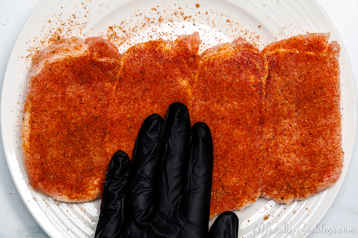 Dry rub seasoning being rubbed and pressed into boneless pork chops on an off-white plate.