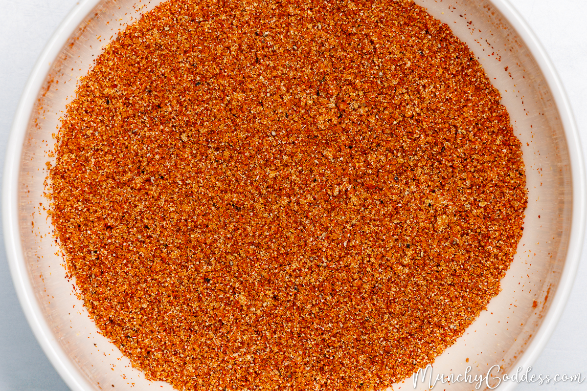 Smoked paprika, chili powder, brown sugar, salt, ground black pepper, garlic powder, and onion powder blended in an off-white bowl.