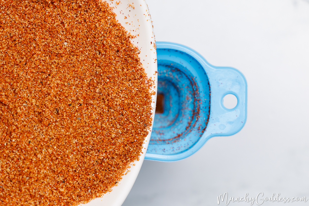 Homemade BBQ seasoning being poured from an off-white bowl into a blue funnel.