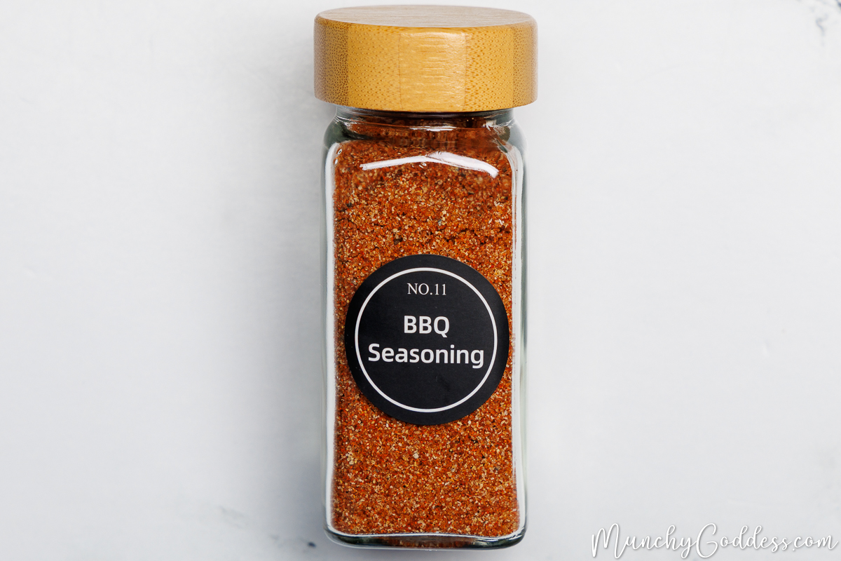 Homemade BBQ seasoning in a glass spice jar with a wooden lid and a black circle label with white font that says "BBQ Seasoning".