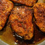 Four perfectly seared, juicy pork chops resting in a skillet, glistening with garlic butter and herbs.