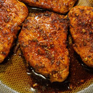 Four perfectly seared, juicy pork chops resting in a skillet, glistening with garlic butter and herbs.