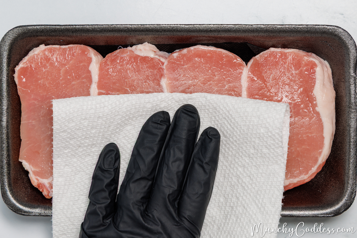 Boneless pork chops in a black foam meat tray being patted dry with a paper towel.