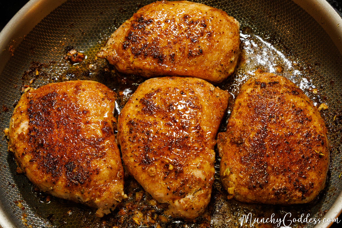 Four finished, deeply browned pork chops glistening with garlic butter in a skillet.